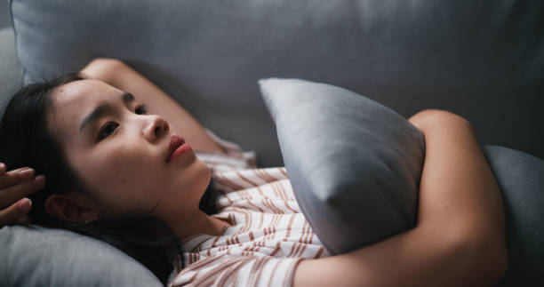 istock Pensive depressed young Asian woman lying on sofa at home looking at ceiling thinking pondering 1621998356