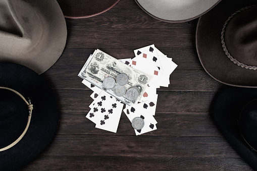 Old west hats with playing card with papers money and silver coins on table. Top view.