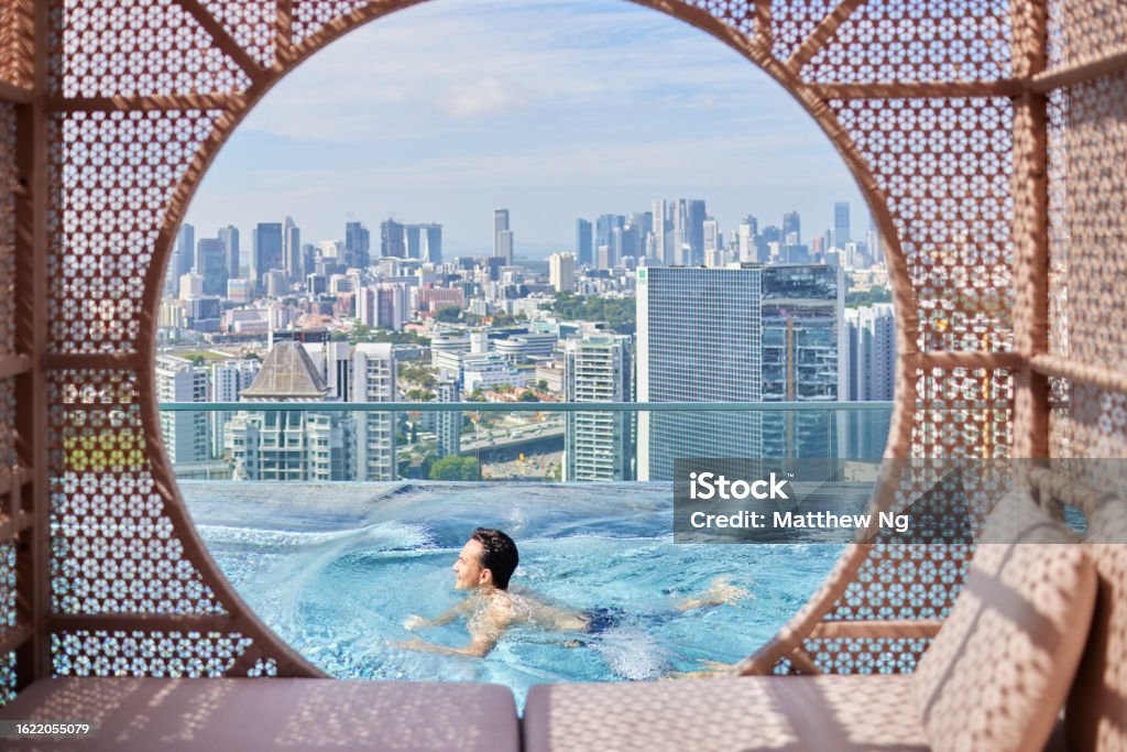 Attractive asian man swimming and doing laps at infinity pool with city skyline Swimming Pool Stock Photo