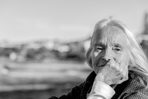Black and white portrait of senior woman with and on chin, outdoor, background with copy space, full frame horizontal composition