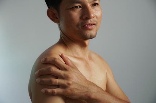 Man recovers from shoulder pain by applying painkiller cream.