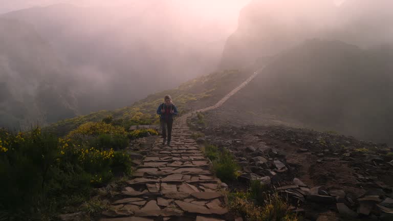 Drone point of view of female hiker moving up the rocky stairs on a mountain.