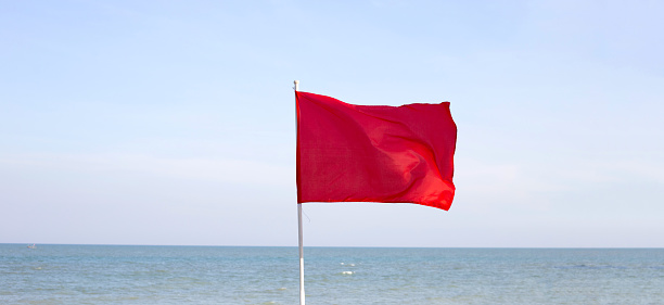 Flapping red flag indicates a warning of dangerous seas and currents with high winds and strong waves along the sandy beach at Son Serra de Marina, Majorca, Balearic Islands, Spain