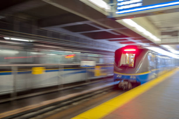 Two blurred motion, fully automated self-driving light rapid transit trains, entering and exiting an above ground station.  Vancouver, British Columbia, Canada.