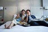 Asian couple enjoying room service on the bed in the comforts of their hotel room