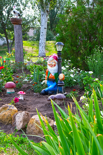 Part of the garden with a ceramic garden gnome. Landscaping in the summer garden.