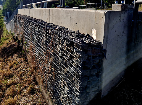 the unsightly concrete wall holding up the slope of the road is lined with a gabion filled with natural stones. the appearance of the lining is more natural, leaching, lining