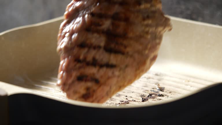 Using tongs to hold the pork steak turned over to the other side on a hot pan in the kitchen at a restaurant.