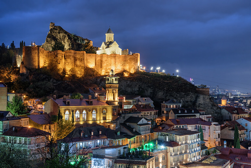 Evening view of Old Town of Tbilisi, Georgia. Narikala Fortress with Saint Nicholas Orthodox Church is visible on blue sky background. Tbilisi is a popular tourist destination of the Caucasus region.