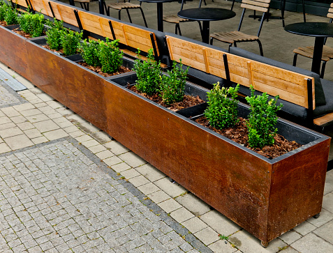 brown flower pots in the garden, park filled substrate. the surface of the flowerpot is intentionally rusty in design. soil, bushes in a row cover the front garden of the pub