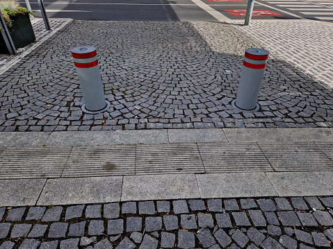 automatic barriers in square cylinder with a hemisphere on top. granite curbs as stops at the parking lot. chain decorative fence against a colony of pedestrians and vehicles with a stone bollard