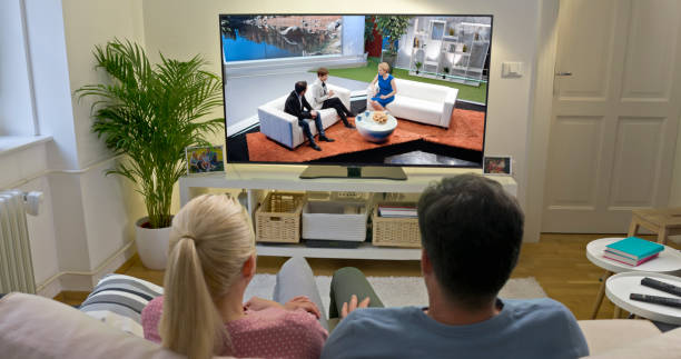 Mature couple watching TV at home Rear view of mature couple watching television show while sitting on sofa in living room. television show stock pictures, royalty-free photos & images