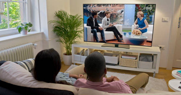 Couple watching TV at home Rear view of couple watching television show while sitting on sofa in living room. television show stock pictures, royalty-free photos & images