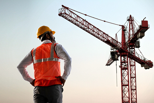 Tower cranes and high-rise buildings silhouettes under construction at construction site at blue clear sky background. Shooting the building new houses in the city