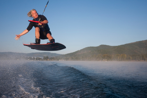A wakeboarder is catching air in an early morning session as fog slowly lifts in the background.
