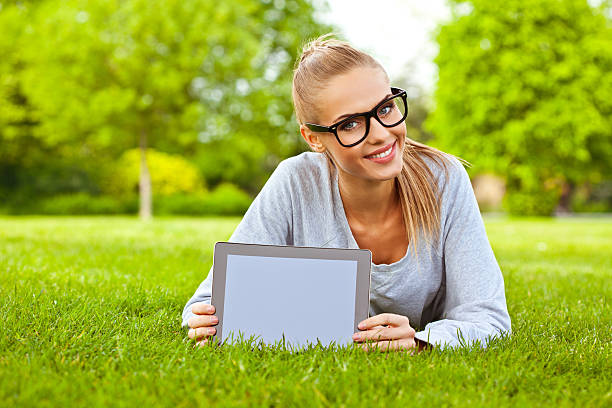 молодая женщина с планшета в парке - glasses grass women lying on front стоковые фото и изображения