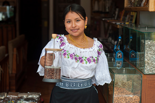 young woman in the doorway of her local business smiling at camera holding a container full of coffee beans. High quality photo