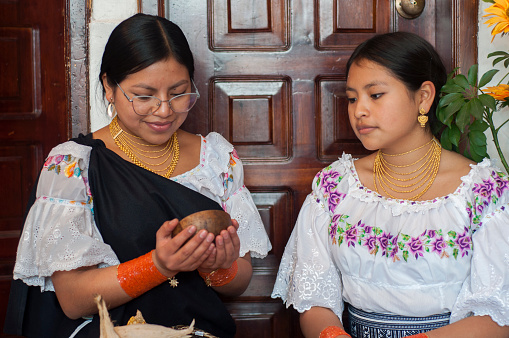 two indigenous sisters sitting in their home sharing a bowl from the otavalo community. High quality photo