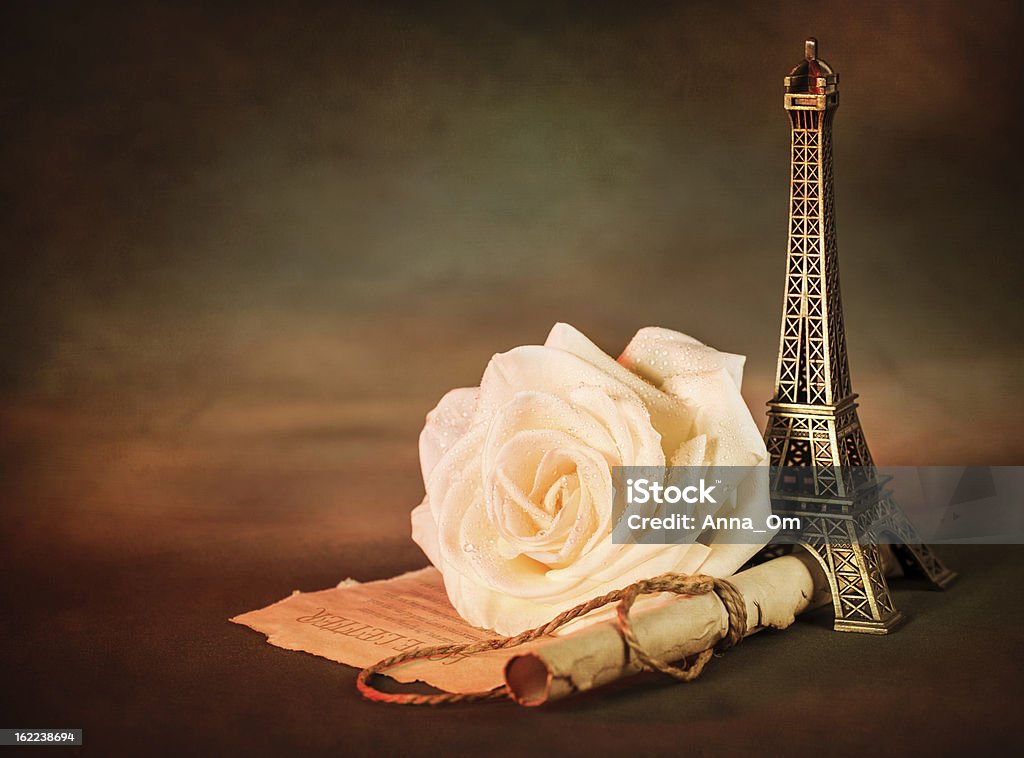 Rose and paper scroll Picture of beautiful still life, old paper scroll with white rose on the table and little Eiffel tower souvenir, dark grunge background, retro style photo, love letter, romantic poem, Valentines day Alphabet Stock Photo