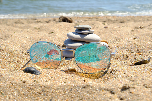 Sunglasses and Pebble tower balance harmony stones arrangment on sea beach coastline.