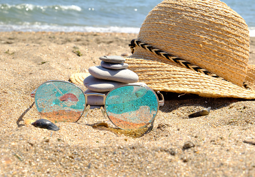 Sunglasses, straw hat and Pebble tower balance harmony stones arrangment on sea beach coastline.