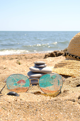 Sunglasses, straw hat and Pebble tower balance harmony stones arrangment on sea beach coastline.