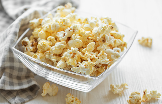 Close up of glass bowl full of popcorn against black background.