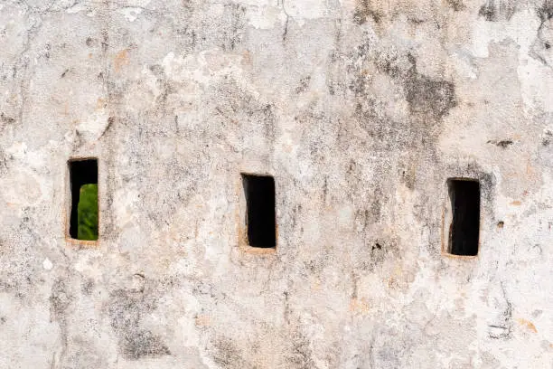 Photo of Loopholes and arrowslits on the white wall of a fort