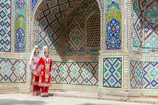 Young Uzbek women dancers in red national clothes. Folk dance against Nodir Devonbegi Madrasah. Travelling and culture concept. April 20, 2023 - Bukhara, Uzbekistan