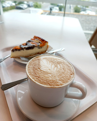 A piece of tangerine pie and a mug of cappuccino on the table by the window in the cafe. High quality photo