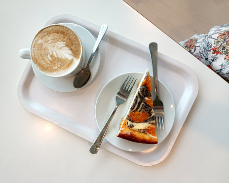 mug of cappucci with a pattern and a piece of cake on a white tray on a table. High quality photo