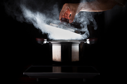 hand open hot boil pot on magnetic oven against black background