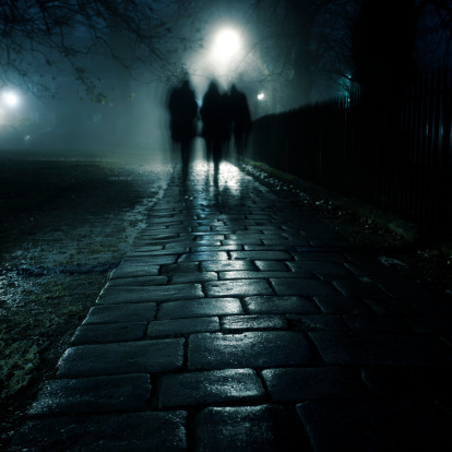 Three people walking on a dark sidewalk in the evening fog