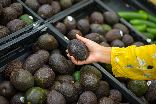 Person holding a hass avocado in a supermarket.