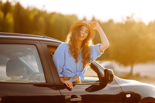 Smiling woman from the window of the car enjoys nature, you feel freedom while traveling by car. Car travel, sunset light. Active lifestyle.