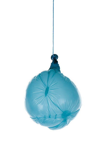 a little boy with curly hair in a straw hat sitting in a basket of a blue balloon smiles against the background of grass and gets ready to fly.
