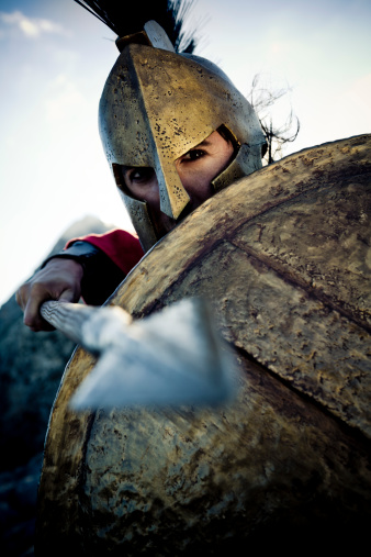 Portrait of Spartan warrior in defense position, selective focus, very creative color retouching to underline the ancient time,vignetting and added noise