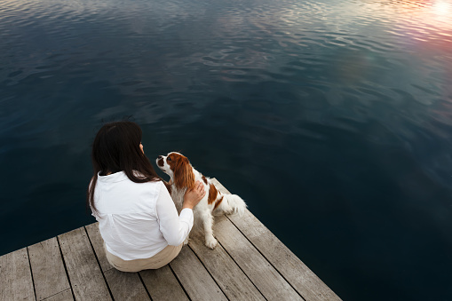 Young woman sitting by the lake with her dog