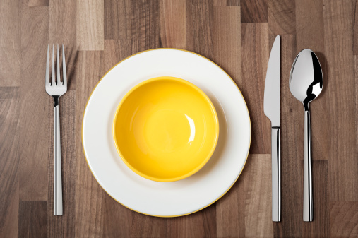 Empty yellow soup bowl and fork,spoon and table knife isolated on wooden table. Include clipping path.