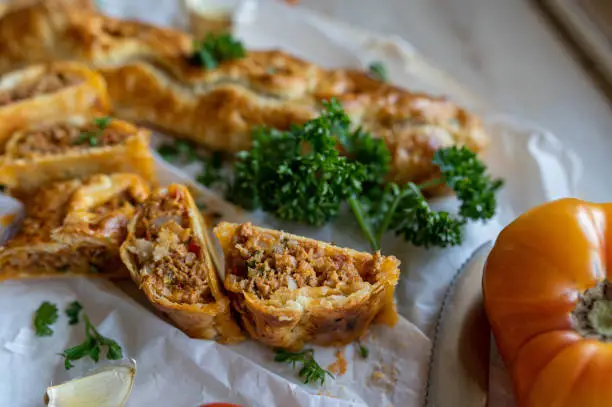 Delicious filled puff pastry rolls or pockets with spice minced meat filling. Served whole and sliced with cross section view on kitchen counter background. Closeup with selective focus