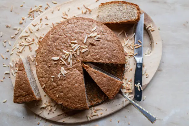 Homemade gluten free and fluffy sponge cake with almonds. Served whole and slice with cake server and knife on light wooden cutting board isolated on a table. Top view with copy space
