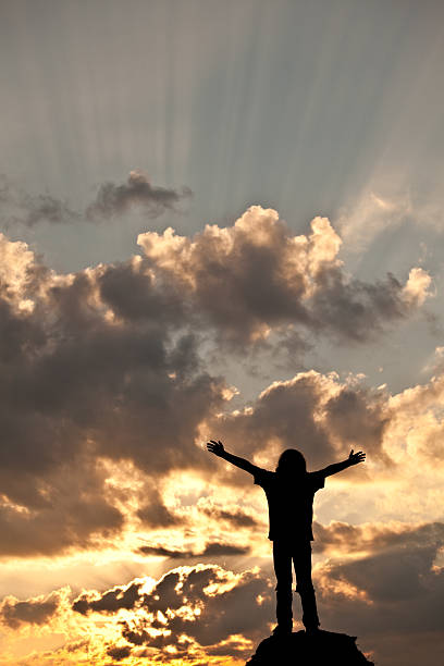 Happy Child in Worship A happy child raising his arms to the sky at sunset. Vertical colour image. Copyspace. Worship concept. Silhouette. Natural God beams in the sky. religion sunbeam one person children only stock pictures, royalty-free photos & images