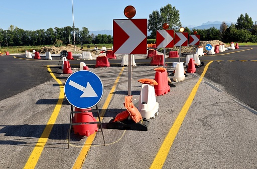 Circle and square directional road signs with warning lights and red and white plastic barriers in front of a roundabout under construction. Roadworks,  background for copy space.