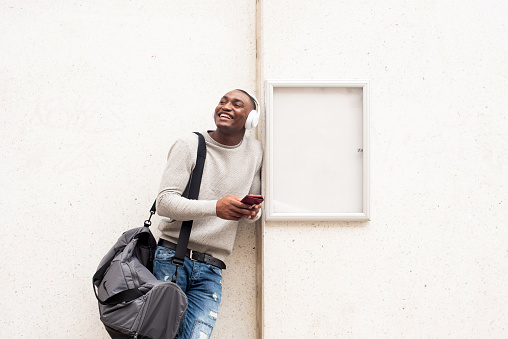 Portrait happy African american man holding cellphone and listening to music with headphones