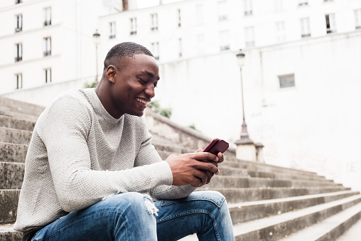 Side portrait smiling African american man sitting outside in city using mobile phone