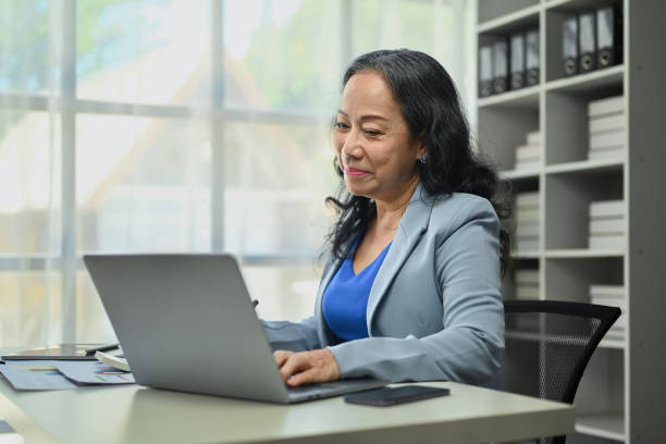 istock Beautiful mature businesswoman using laptop working with statistics documents at modern office. 1622559566