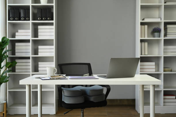 istock Modern office interior with laptop, documents and coffee cup on white table against gray wall. 1622559963
