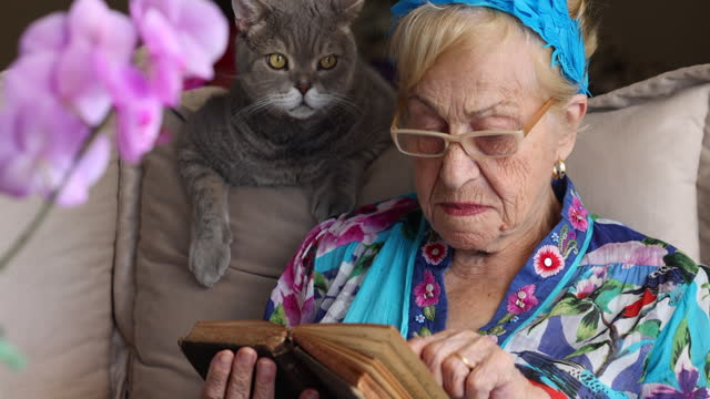 Beautiful senior woman reading old book and her cat at home.