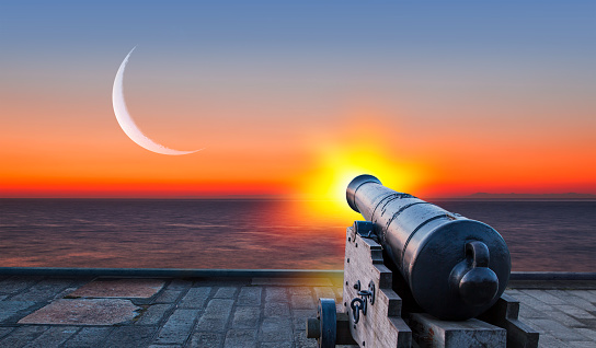 Ramadan kareem concept - Ramadan kareem cannon with crescent - Night sky with moon in the clouds at sunset