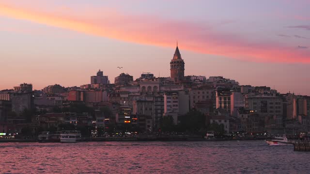 Panoramic view of the Beyoglu district with illuminated Galata Tower at sunset. The ferry with tourists is floating along the Golden Horn waterway inlet of the Bosphorus